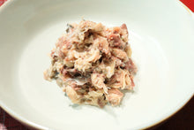 画像をギャラリービューアに読み込む, 熊野灘や伊勢志摩産の天然魚の無添加レトルトフレークお魚ごはんがお皿に盛り付けられている。袋の上から指でほぐした小魚がフレーク状になっており、骨もワタも入っている様子が確認できる。